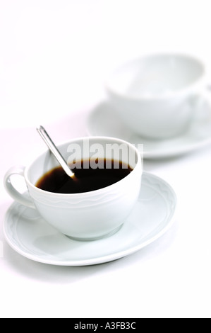 ZWEI WEIßE TASSEN MIT KAFFEE UND LÖFFEL AUF WEIßEM HINTERGRUND MONOTONE Stockfoto
