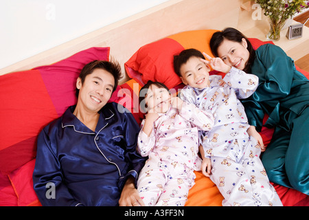 Porträt von zwei Eltern mit ihren zwei Kindern auf dem Bett liegend Stockfoto