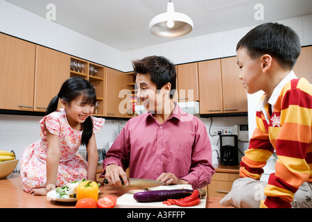 Mitte erwachsener Mann und seinen Kindern Schneiden von Gemüse auf eine Küchentheke Stockfoto