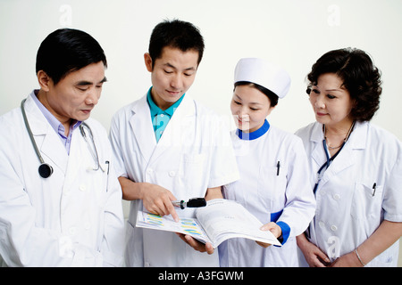 Nahaufnahme von zwei männlichen Ärzte und eine Ärztin mit einer weiblichen Krankenschwester diskutieren einen Bericht Stockfoto
