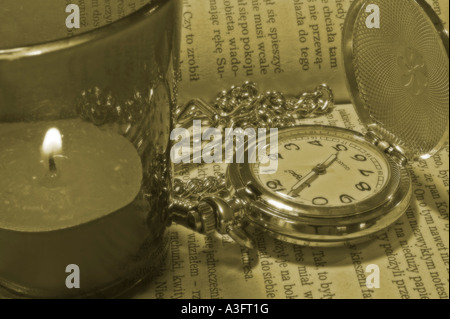 Stillleben mit einem alten Stil Tasche Uhr Deckel und Kette mit einer Kerze auf ein offenes Buch in sepia Stockfoto