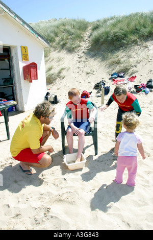 Ein RNLI Strand Rettungsschwimmer behandelt ein junges Mitglied der Holywell Bay Surfclub für ein Weber stechen Cornwall UK Stockfoto