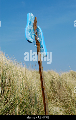 Blaue Flip-Flops ruht auf einem Holzstab unter Sanddünen an einem Sommertag Stockfoto