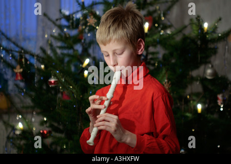 kleiner Junge spielt des Recorders vor einem Weihnachtsbaum Stockfoto