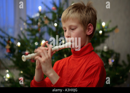 kleiner Junge spielt des Recorders vor einem Weihnachtsbaum Stockfoto