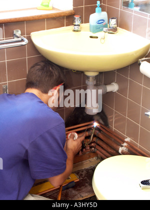 Zurück von beaufsichtigten Auszubildenden Klempnerarbeiten in Wohneigentum freigegebenes Haus erneuert Zentralheizungssystem, beugt sich nach unten Arbeiten unter dem Becken Großbritannien Stockfoto