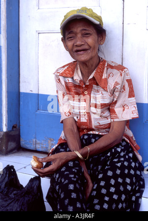 Lächelnd zahnlose Obdachlose Essen einen kleinen Kuchen am Straßenrand in Madiun Ost-Java Indonesien Stockfoto