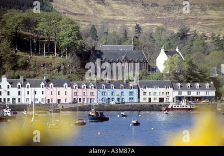 Isle of Skye mit Blick über den Hafen auf eine Reihe von Häusern am Wasser und festgemachten Booten, gesehen durch gelben, unscharf im Fokus stehenden Ginster an einem sonnigen Tag in Portree Town Stockfoto