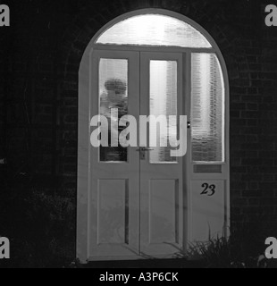 Monochromes Bild des jungen Paares küssen im beleuchteten Veranda hinter Tür Stockfoto