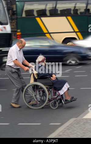 Mann schob eine alte Frau im Rollstuhl auf der anderen Straßenseite Stockfoto