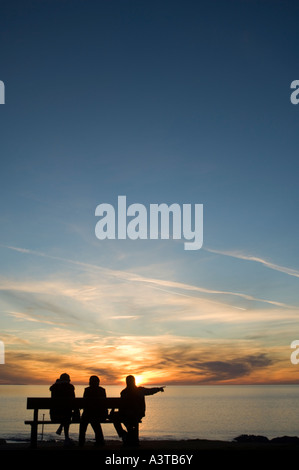 Silhouette der drei Frauen saßen auf Bank Blick auf Sonnenuntergang über Aberystwyth promenade Stockfoto