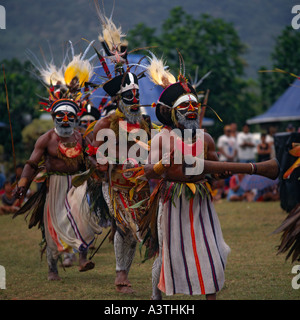 Männliche Engi Stammesangehörigen aus Papua Neuguinea tanzen in schwarz & gefiederten Kopfschmuck und tragen große Medaillons mit aufgemalten Gesichtern Stockfoto