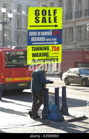 Regent Street-Pflaster-Mann liest Buch & Holding tragbare Werbung Panel Förderung aus der ausgetretenen Seite drehen Geschäfte Stockfoto