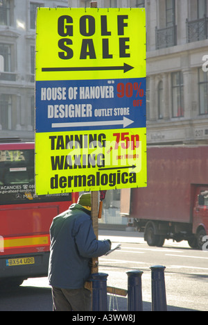 Regent Street-Pflaster-Mann liest Buch & Holding tragbare Werbung Panel Förderung aus der ausgetretenen Seite drehen Geschäfte Stockfoto