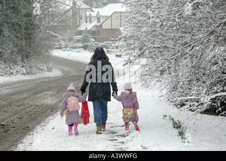 Winter Street Szene kleine Kinder auf dem Bürgersteig im Schnee Hände mit der Mutter auf dem kalten Morgenspaziergang zum Dorf halten Schule Essex England Großbritannien Stockfoto