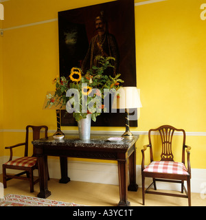 Sonnenblumen auf Konsole Tisch mit zwei Stühlen unter Artwork auf gelbe Wand Stockfoto