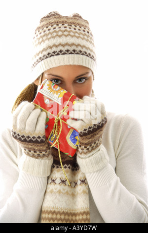 Junge Frau, die kokett Weihnachtsgeschenk vor ihr Gesicht halten Stockfoto