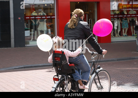 Frau mit Kind auf dem Soziussitz für ihr Fahrrad. Das Kind hält Luftballons Stockfoto