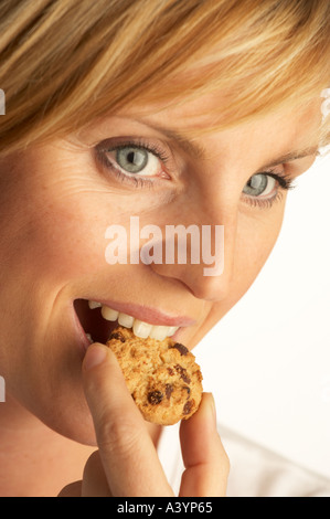 GESUNDEN ATTRAKTIVE JUNGE, BLONDE FRAU BEIßEN IN CHOCOLATE CHIP COOKIE Stockfoto