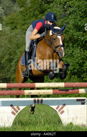 Junge Dame Fahrer mit einem Reiten Hut und einen Körperschutz beim Springen auf Rückseite ein pony Stockfoto