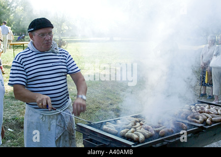 MANN KOCHEN WÜRSTCHEN AUF EINEM GRILL TADEN BRETAGNE FRANKREICH Stockfoto