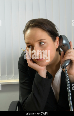 Müde Managerin, die ihr Kinn in der Hand ruht, während sie an einem Festnetztelefon hört. Stockfoto