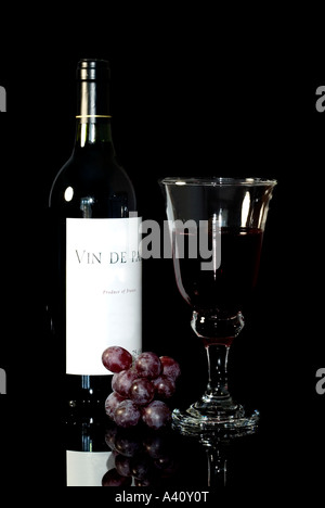 Wein-Stillleben Landwein Flasche Vin de Pays Glas und roten Trauben schwarzer Hintergrund mit Reflexion Stockfoto