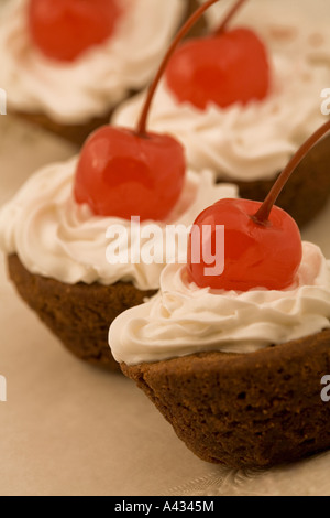 Kleine Schokoladen Cupcakes überstiegen mit gepeitschter Creme Sahnehäubchen und einer Maraschino-Kirsche. Stockfoto