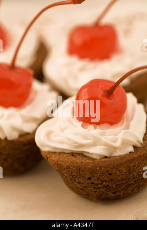 Kleine Schokoladen Cupcakes überstiegen mit gepeitschter Creme Sahnehäubchen und einer Maraschino-Kirsche. Stockfoto
