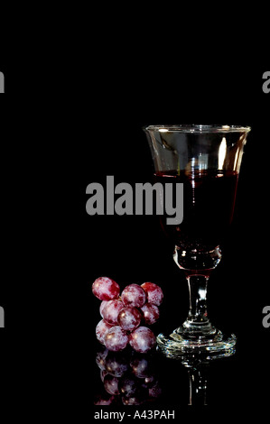 Glas Rot Wein und roten Trauben auf einem schwarzen Hintergrund mit Reflexion Stockfoto