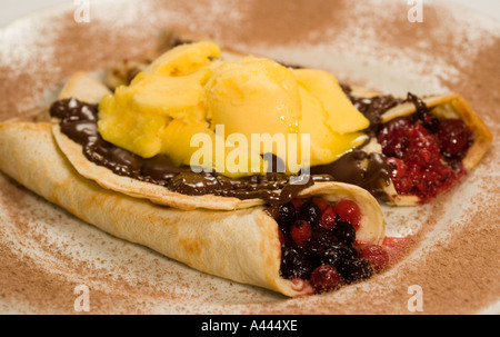 Zwei Pfannkuchen gefüllt mit Obst, beträufelt mit geschmolzener Schokolade und gekrönt mit Mango-Sorbet serviert auf einer Schokolade bestäubt Platte Stockfoto