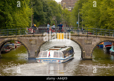 Kanalboot mit Touristen auf einem Ausflug unter einer niedrigen Fußgängerbrücke. Amsterdam Niederlande. Stockfoto