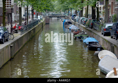 Schmaler Kanal von einer Brücke aus gesehen, mit Blick auf die nächste Brücke mit kleinen Booten, die entlang der Seite vertäut sind. Amsterdam. Niederlande Stockfoto