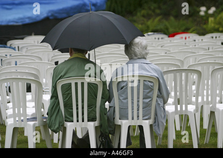 Zwei ältere englische Rentner sitzen auf Stühlen im Regen warten auf einer Open-Air-Oper. Stockfoto