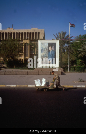 ein Mann schiebt einem Handwagen zu Markey vor Plakat zeigt ein Bild von Saddam Hussein-Bagdad-Irak Stockfoto