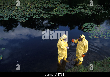 Zwei Arbeiter in Schutzanzügen testen chemischen Niveaus in einem Körper des Wassers Stockfoto