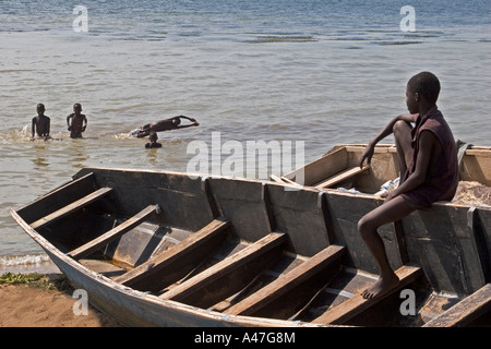 Lakeside Szene von Fischerbooten mit jungen spielen und Schwimmen im Wasser am Ufer von Lake Albert, Nord-Uganda, E Afrika Stockfoto