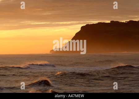 Klippen bei Dämmerung fallen in eine energetische Meer beleuchtet von warmen Farbtönen von einem nebligen Sonnenaufgang alte Spitze Klippe am Ravenscar in North Yorkshire Stockfoto