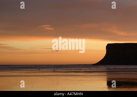 Aussicht auf den Strand bei Saltburn in North Yorkshire mit gold vor Sonnenaufgang Farben Himmel spiegelt sich auf nassem Sand mit Blick auf Jagd Cliff Stockfoto