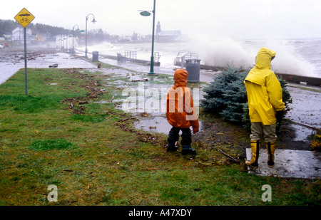 Zwei Kinder beobachten große Wellen schlagen das Dorf an der Küste von St. Luce in Quebec Stockfoto