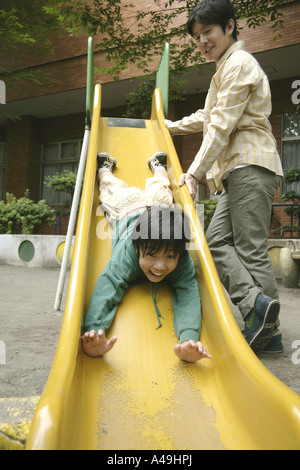 Niedrigen Winkel Ansicht eines jungen Rutschen auf einer Folie mit seinem Vater neben ihm stehenden Stockfoto