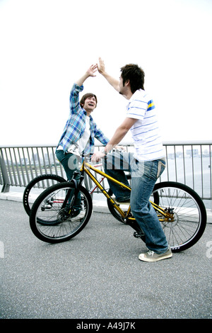 Profil von zwei jungen Männern auf einem Fahrrad sitzen und geben hohe fünf Stockfoto