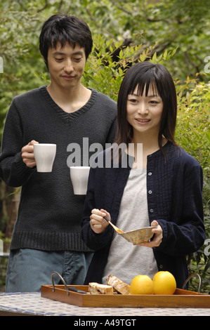 Junge Frau hält eine Schüssel geben und eine Gabel mit einem jungen Mann hinter ihr halten Kaffee Tassen Stockfoto