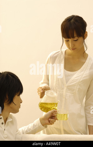 Junge Frau in eine junger Mann s Teetasse Tee gießen Stockfoto