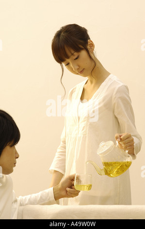 Junge Frau in eine junger Mann s Teetasse Tee gießen Stockfoto