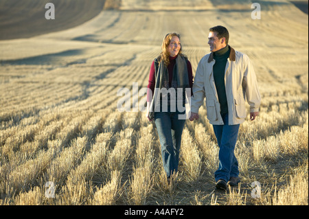Paar Hand in Hand spazieren durch Felder golden gemähtes Gras im Herbst Colorado am frühen Morgen lächelnd Stockfoto