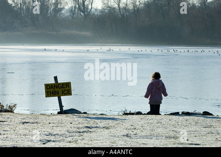 Ein Kind blickt auf einem vereisten Teich neben ein Schild Warnung vor dünnem Eis. Stockfoto