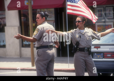 Zwei Hispanic PolizistInnen, Direktverkehre in San Diego, CA. amerikanische Flagge im Hintergrund. Stockfoto