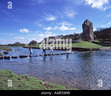 Eine Gruppe von Mädchen überquert die Trittsteine über den Fluss Ewenny zum Ogmore Castle im Tal von Glamorgan, Wales vor einem blauen Himmel mit wispy Wolke Stockfoto