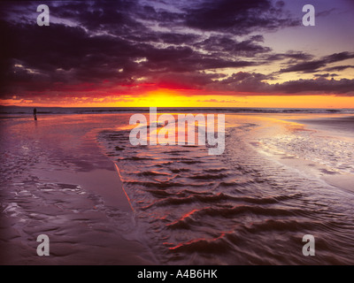 Dramatischer Sonnenuntergang mit brillantem Horizont, der sich in nassem Sand und einem Bach widerspiegelt, der über den Strand von Dunraven Bay, Southerndown, Vale of Glamorgan fließt Stockfoto
